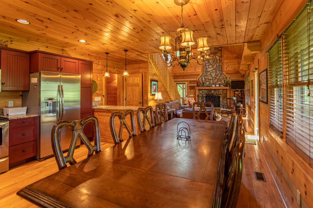 A spacious dining area featuring a large wooden table, a striking chandelier, and a stone fireplace. The setting is warm and welcoming, ideal for family gatherings and sharing stories after a day exploring the mountains with pets.