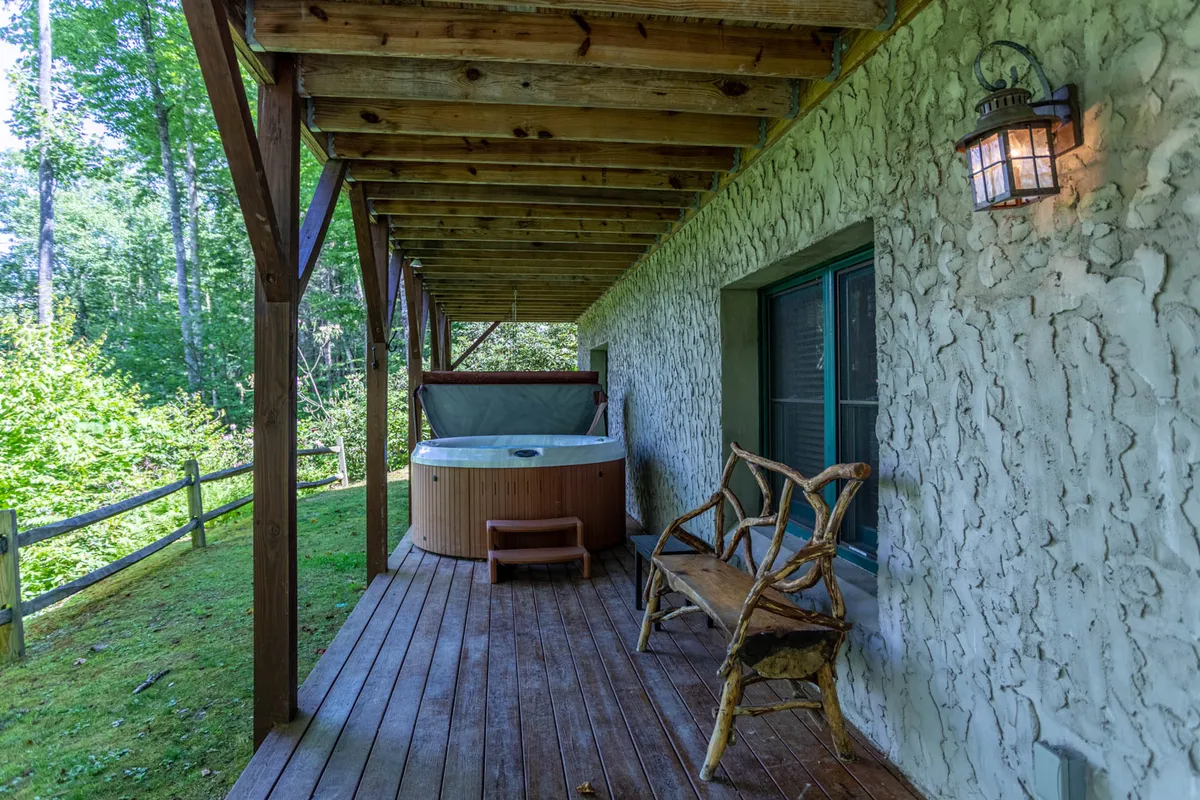 An outdoor hot tub sits on a wooden deck surrounded by lush greenery. A wooden bench offers additional seating, and the tranquil setting is perfect for relaxation after a day of adventure. The setup suggests both comfort and immediate access to the natural environment.