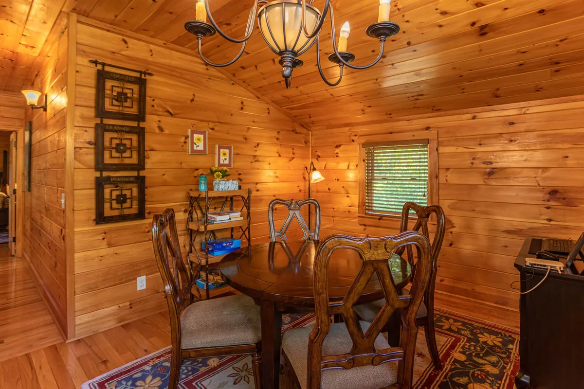 A spacious dining area with a wooden table, chandelier, decorative wall art, and comfortable wooden chairs. The space is set up for communal meals, game nights, and intimate gatherings, suggesting flexibility for group activities.