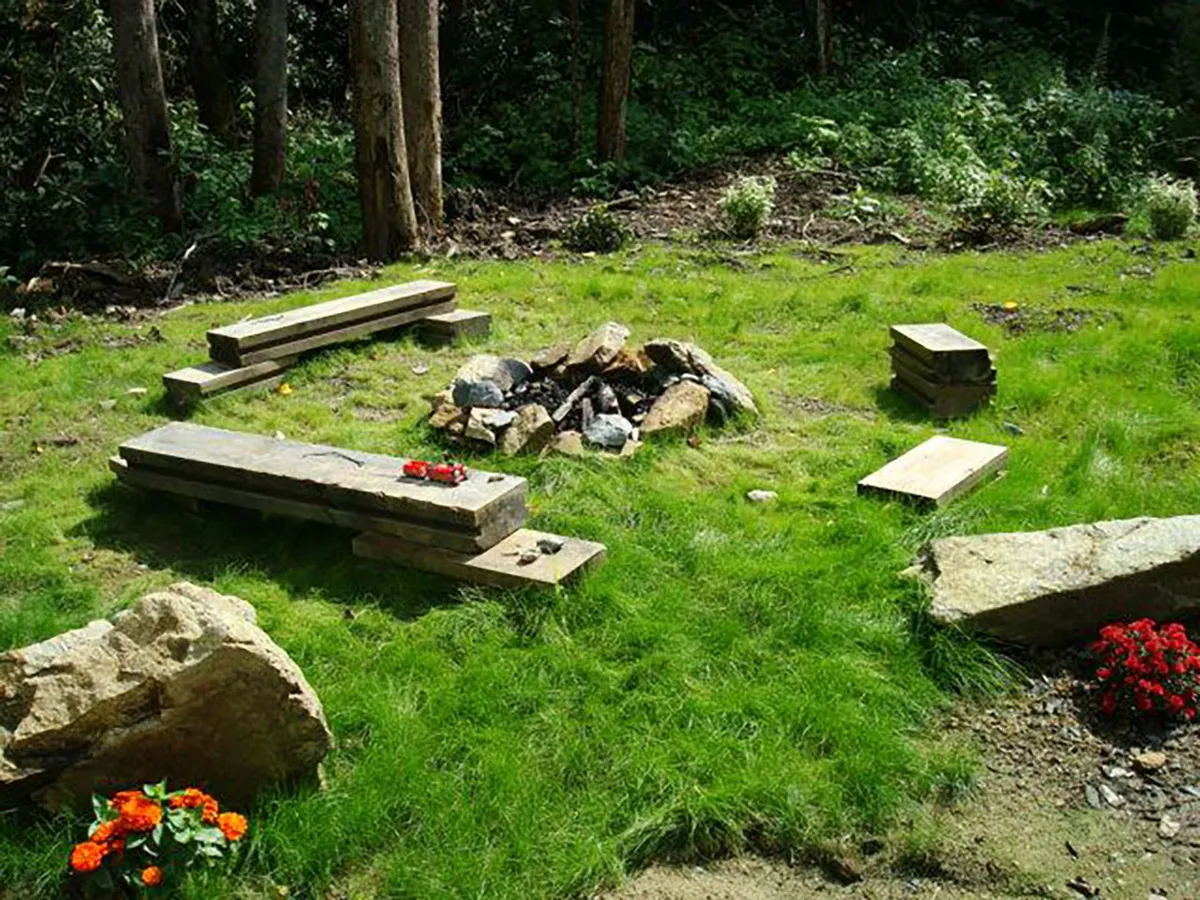 A close-up of the fire pit ringed by wooden benches, surrounded by flower beds and open lawn. The image captures a setting ideal for campfire gatherings, storytelling, and outdoor relaxation as the sun sets.