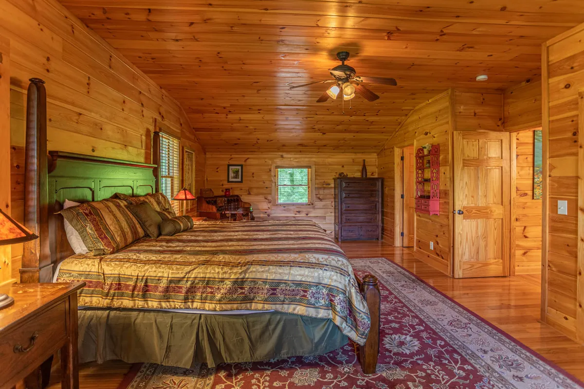 A tranquil shared bedroom with two large beds, wood-paneled ceiling and walls, an ornate area rug, and decorative lamps. The natural light and seating arrangement invite group relaxation and late-night conversations.