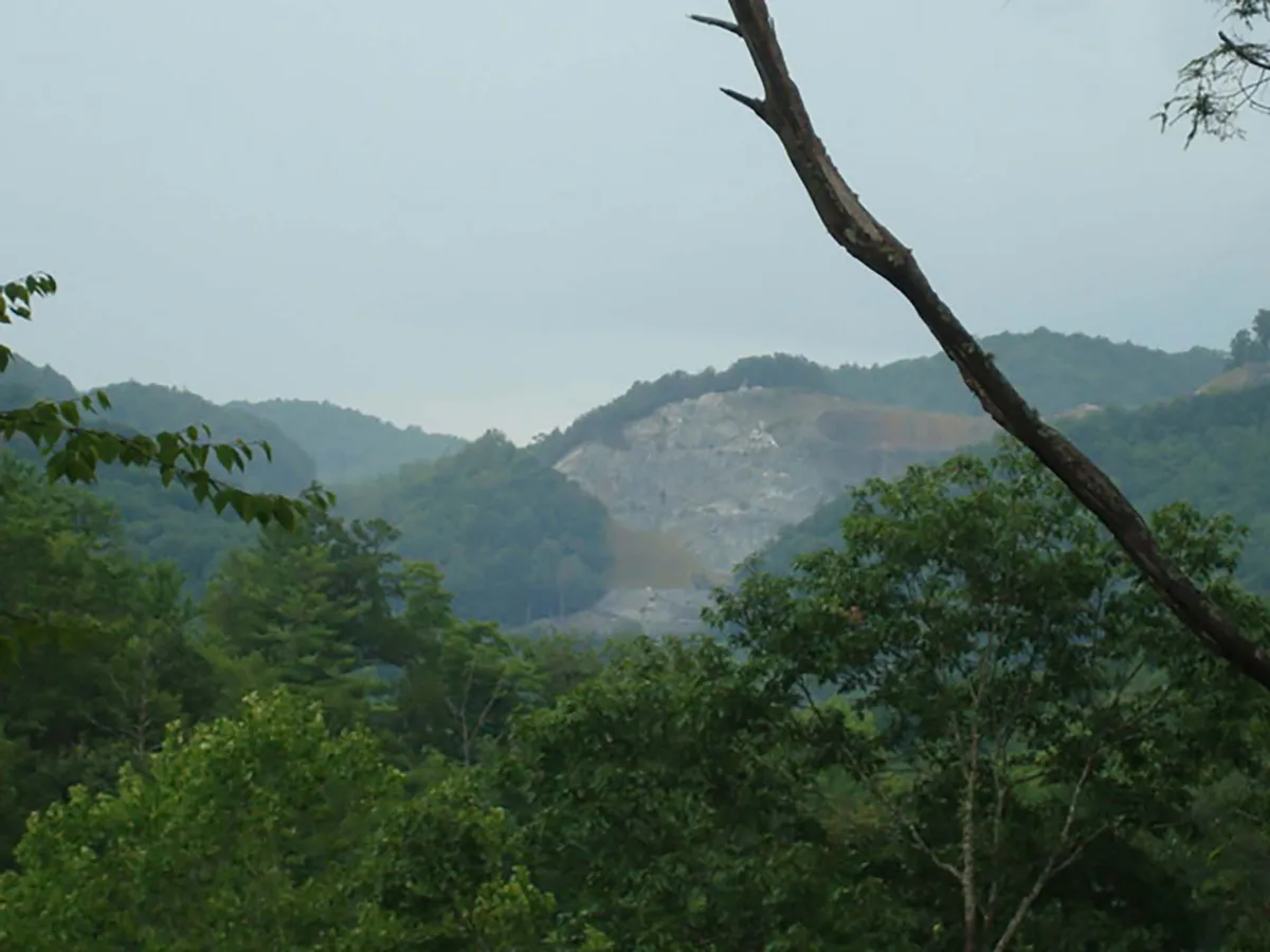 This image captures a sweeping view of a mountainous landscape in the Blue Ridge region, with a quarry visible in the distance and abundant trees in the foreground. The natural terrain and dramatic slopes evoke the grandeur of the surrounding wilderness and opportunities for hiking, wildlife spotting, and nature observation.