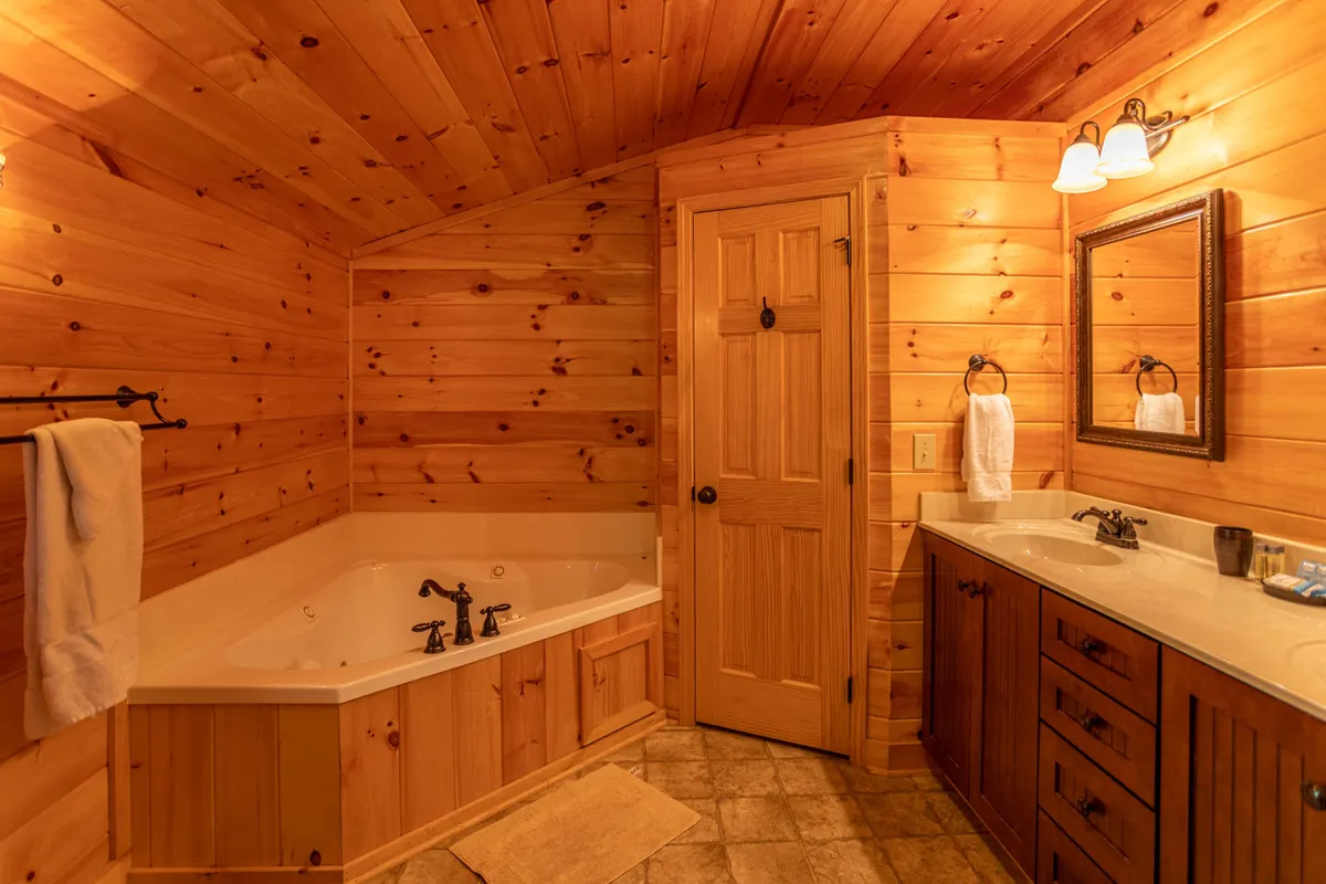 A bathroom sanctuary with a deep soaking tub, rustic wood walls, sink area, and large mirror. The space is tranquil and intimate, ideal for unwinding after a day of adventure.