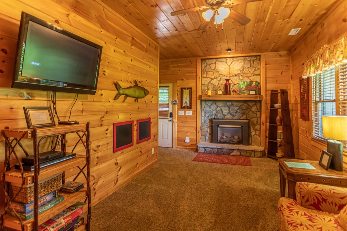 A cozy den with a prominent stone fireplace, wooden walls, comfortable seating, and a television. The space is perfect for relaxing with family, watching movies, or enjoying board games by the fire, capturing the warmth and togetherness described in the text.