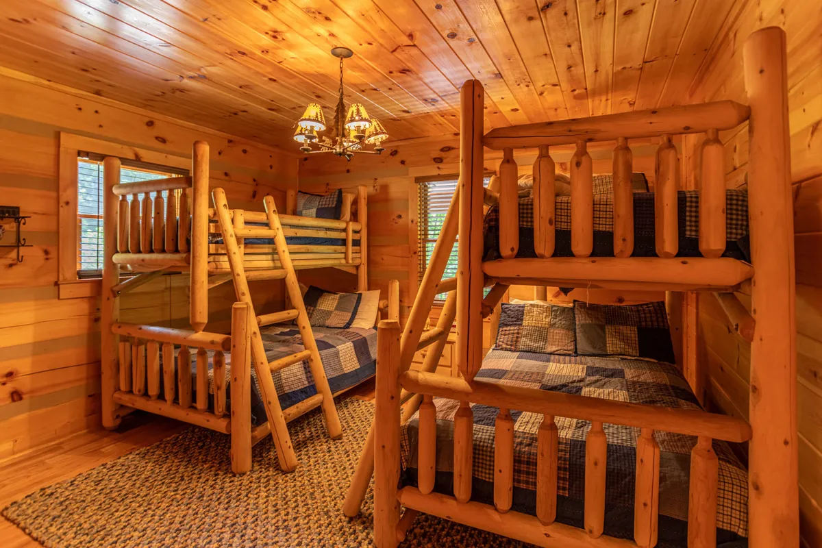 A playful bunk room with wooden paneling, charming chandelier, and sturdy bunk beds. The space is designed for kids or cousins, with a warm, storybook feel ideal for sleepovers and shared adventures.