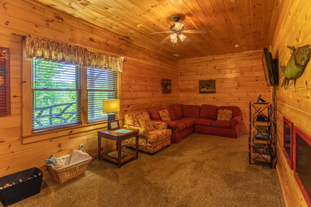 A cozy living room with a sofa seating area positioned by a large window that offers views of the outdoors. The space features a table lamp and a casual atmosphere, inviting relaxation and socializing while staying connected to the natural environment outside.