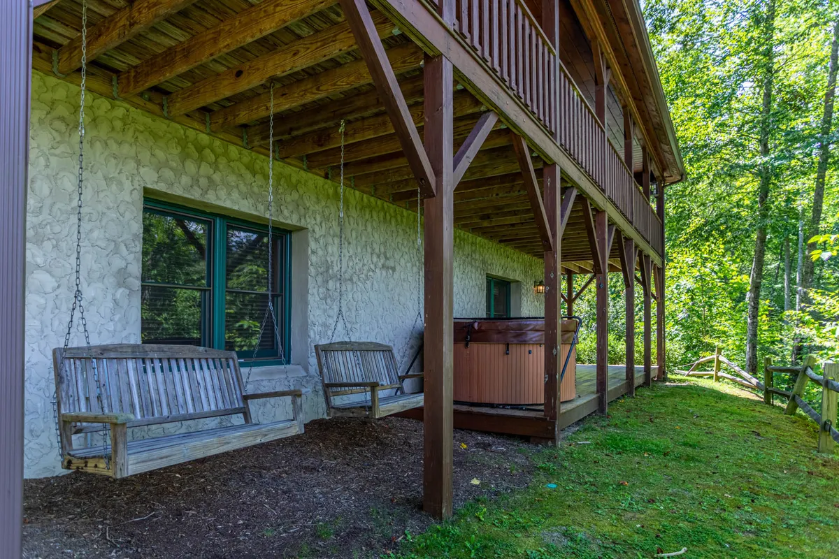 A covered outdoor area featuring both hanging swings and a hot tub, with a view of the wooden structure and surrounding greenery. This inviting spot blends relaxation with the fresh mountain air, ideal for unwinding or stargazing as described in the section.