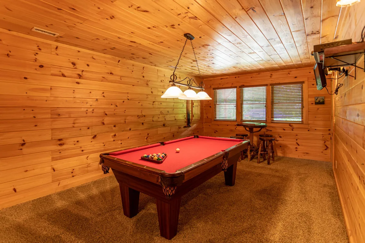 A spacious game room featuring a pool table under a hanging light fixture, with windows providing natural light. The relaxed atmosphere is ideal for friendly gatherings and lively game nights, emphasizing the entertainment options mentioned in the section.